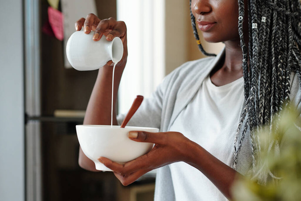 Γυναίκα ρίχνει φρέσκο γάλα ή κρέμα γάλακτος σε μπολ με μούσλι ή granola - Φωτογραφία, εικόνα