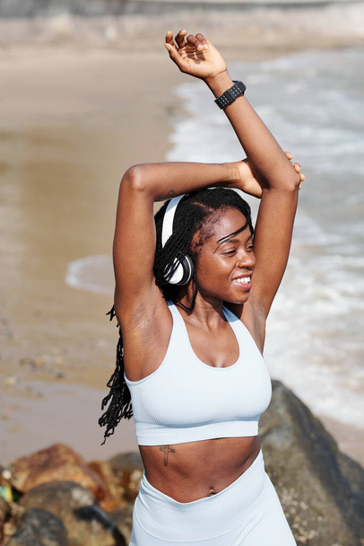Счастливый возбужденный подходит молодой спортсменке, стоящей на пляже и наслаждаясь морским бризом после тренировки - Фото, изображение