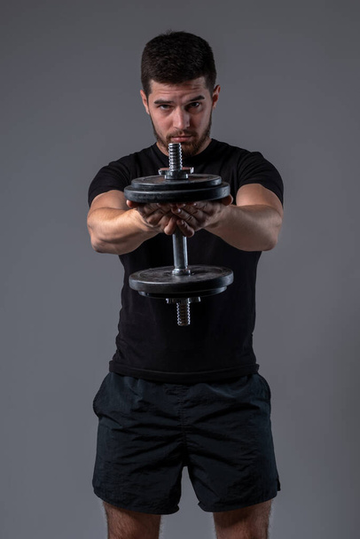 Athletic guy performing one dumbbell front raise - Fotoğraf, Görsel