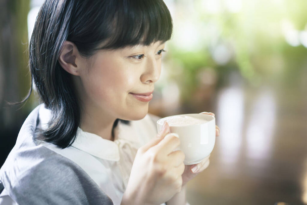 Νεαρή γυναίκα πίνει καφέ σε ζεστή ατμόσφαιρα - Φωτογραφία, εικόνα