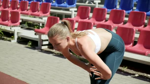 young fit busty woman with ponytail in sportswear stretching at sports ground - Video