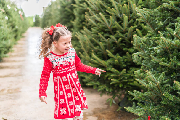 Petite fille en robe rouge à la ferme des arbres de Noël. - Photo, image