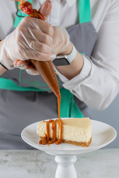 Pastry chef pours caramel on a slice of the freshest cheesecake on a white plate. - Fotoğraf, Görsel