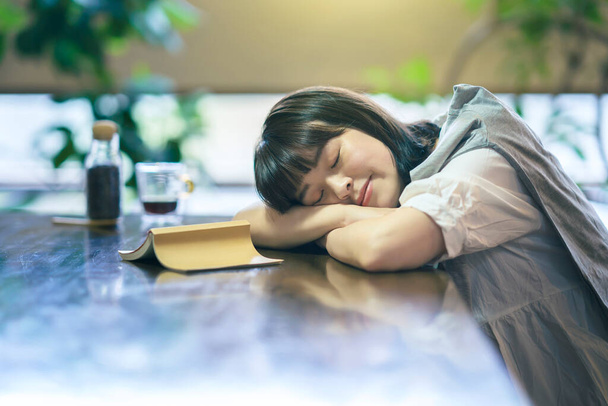 Eine junge Frau schläft in einem mäßig hellen Raum mit einem Buch und einem Glas Kaffee - Foto, Bild