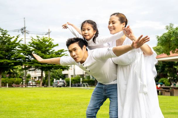 Portrait einer glücklichen asiatischen Familie mit drei Kindern, die zusammen Spaß im Park haben, kleine Tochter, die auf dem Rücken von Vater und Mutter sitzt, beim Gehen lächelt und lustige Momente im Sommerpark zu Hause hat - Foto, Bild