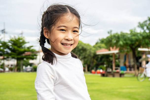 Portrait de petite fille asiatique mignonne debout dans le parc d'été regardant à la caméra souriant joyeusement, Rire enfant, Expressions faciales expressives. - Photo, image