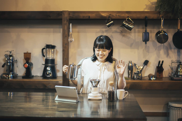Μια νεαρή γυναίκα που φτιάχνει καφέ με ένα χέρι στάζει σε ένα ήρεμο φωτισμένο χώρο - Φωτογραφία, εικόνα