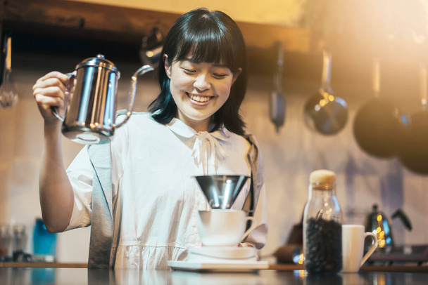 Mladá žena vařící kávu s rukou kape v klidném osvětleném prostoru - Fotografie, Obrázek