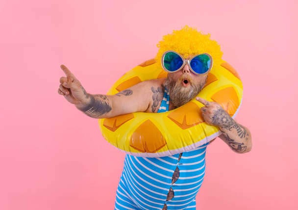Dikke man met pruik in het hoofd is klaar om te zwemmen met een donut levensredder - Foto, afbeelding