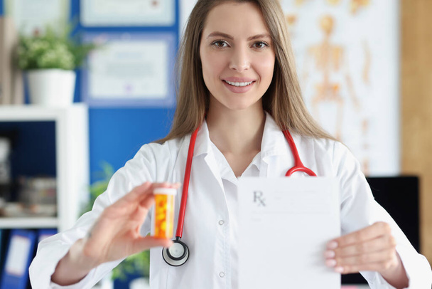 Doctor holding jar of medicines and prescription blank in clinic - Фото, изображение