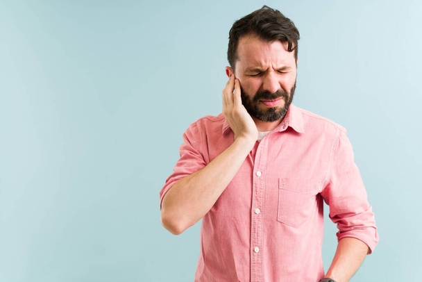 Worried man in his 30s aching and listening to a ringing in his ear. Pained man with touching his ears because of an infection  - Photo, Image