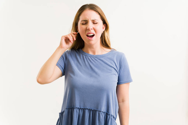 Mujer joven estresada gritando debido al dolor mientras usa hisopos de algodón para limpiar la cera de su oído sucio  - Foto, imagen