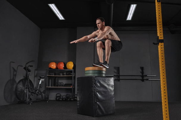 Portrait d'un homme athlétique faisant un exercice de saut en boîte. Crossfit, sport et mode de vie sain concept. Prise de vue d'un jeune homme en train de sauter sur la boîte dans le cadre de la routine d'exercice. Cross, formation fonctionnelle - Photo, image