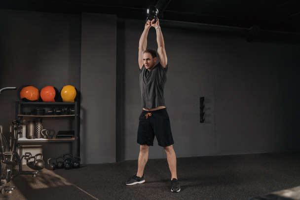 Crossfit gym. Young sportsman doing kettlebell swings at sport fitness club. Copyspace. Muscular strong crossfit man exercising with kettlebell, have weightlift functional training, working out - Photo, Image