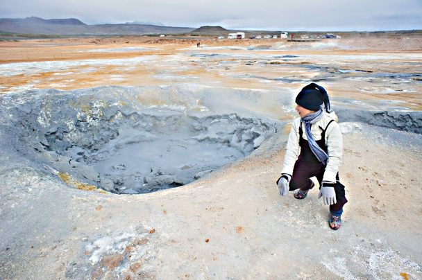 Mujer joven en overoles que viajan en el área geotérmica de Hverir en el norte de Islandia, ollas de barro del volcán hirviendo y suelo gris rojo agrietado, Energía alternativa geotérmica, Namafjall - Foto, Imagen