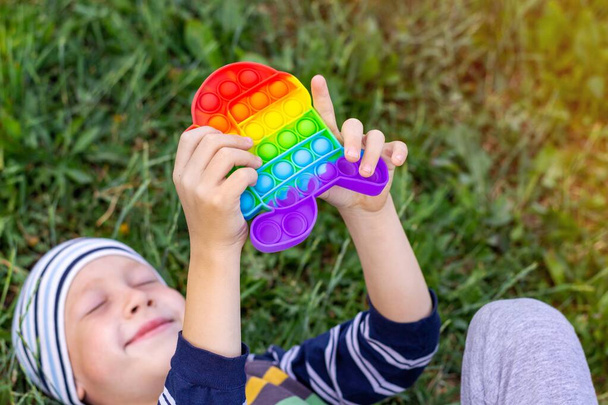The concept of the psychological health of preschool children. Child boy pushing a toy antistress pop it lying on the grass. - 写真・画像