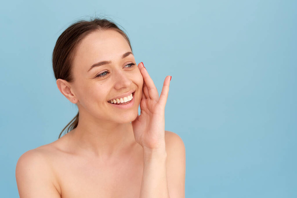 Piękny model o zdrowej skórze dotyka czystej skóry twarzy. Koncepcja spa kosmetycznego, piękna, świeża, czysta kobieca twarz - Zdjęcie, obraz