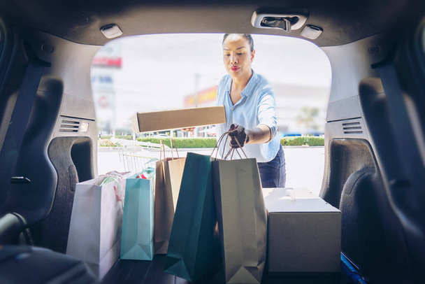 Happy women full paper and tote shopping bags in cart.Colorful bag and brown Box in back car trunk storage.Woman checking and setting the product she bought. Shopping addiction or shopaholic concept. - Fotoğraf, Görsel