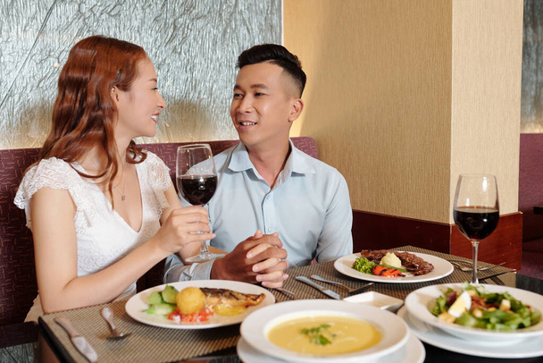 Usmívající se mladý přítel a přítelkyně v lásce drží za ruce při jídle a mluví u stolu restaurace - Fotografie, Obrázek