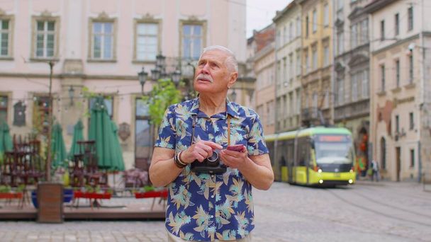 Homme de tourisme élégant âgé à la recherche d'un moyen de trouver un itinéraire en utilisant un smartphone dans la vieille ville de Lviv, Ukraine - Photo, image