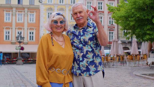 Idosos elegante casal turistas homem mulher olhando aprovadamente para a câmera mostrando ok gesto como sinal - Foto, Imagem