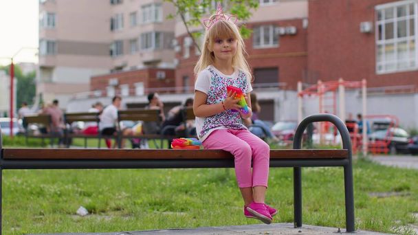 Stijlvol klein kind spelen met trendy pop het zeepbel squishy zintuiglijk speelgoed spel op speelplaats bank - Foto, afbeelding
