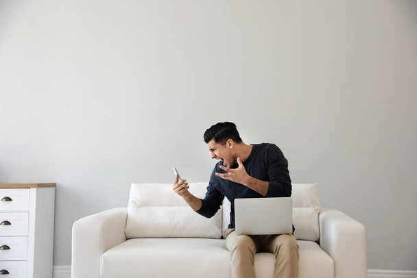 Emotional man with smartphone and laptop at home - Foto, afbeelding