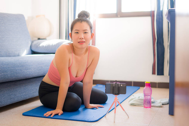 healthy lifestyle portrait of young happy and beautiful Asian Chinese woman smiling sweaty after training workout on yoga mat following online lesson on her phone at home - 写真・画像