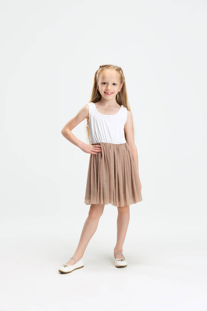 Beautiful little girl in modern stylish dress posing isolated on white studio background. Happy childhood concept. - Photo, Image