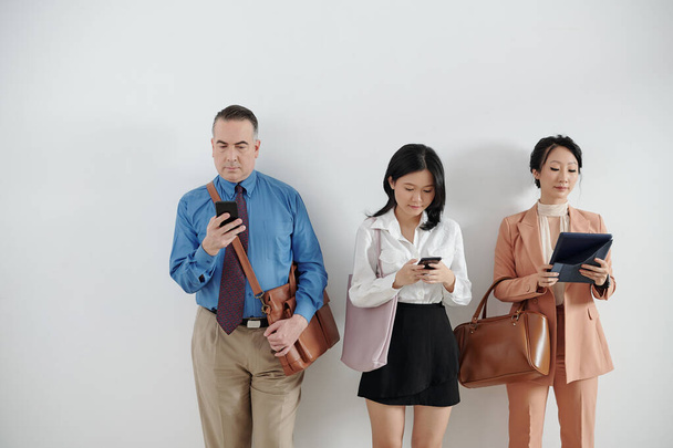 Uchazeči stojí ve frontě, čekají na pracovní pohovor a kontrolují sociální média na chytrých telefonech a tabletech - Fotografie, Obrázek