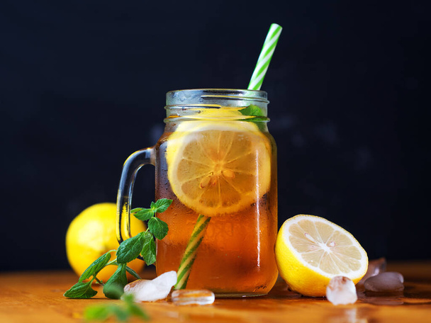 Rinfrescante tè freddo agli agrumi con limone, menta e cubetti di ghiaccio in una tazza di vetro su un tavolo di legno. - Foto, immagini