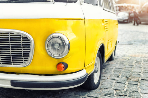 Close-up detail front view of headlight part old vintage bright yellow retro mini bus car van parked in european city center on cobble stone paved road. Fun vehicle for snack delivery sale journey. - Photo, Image