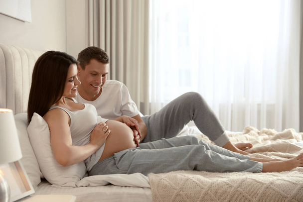 Young pregnant woman with her husband in bedroom - Фото, изображение