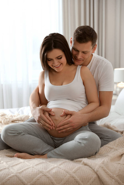 Young pregnant woman with her husband in bedroom - Фото, изображение