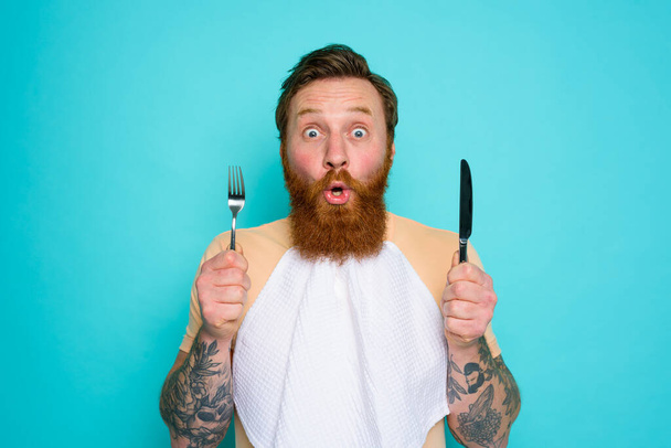 Uomo scioccato con tatuaggi è pronto a mangiare qualcosa con le posate in mano - Foto, immagini