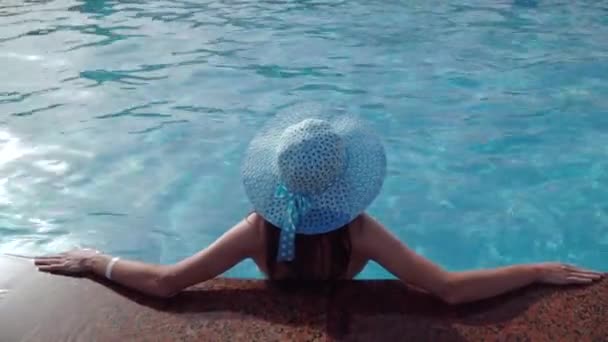Parte posterior de una mujer en sombrero azul apoyado en el borde de la piscina dentro de la piscina cubierta con azulejo mozaico, espacio de copia de plantilla, vista elevada - Metraje, vídeo