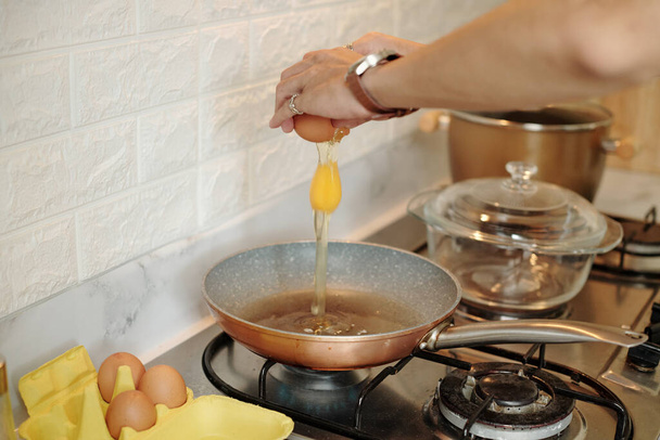 Close-up de homem irreconhecível rachando ovo na panela de cozinhar enquanto prepara ovos fritos no fogão - Foto, Imagem