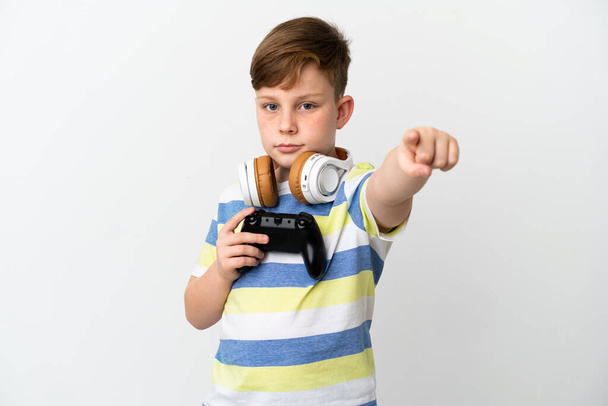 Mały rudy chłopiec trzyma podkładkę gry izolowane na białym tle zaskoczony i wskazując z przodu - Zdjęcie, obraz