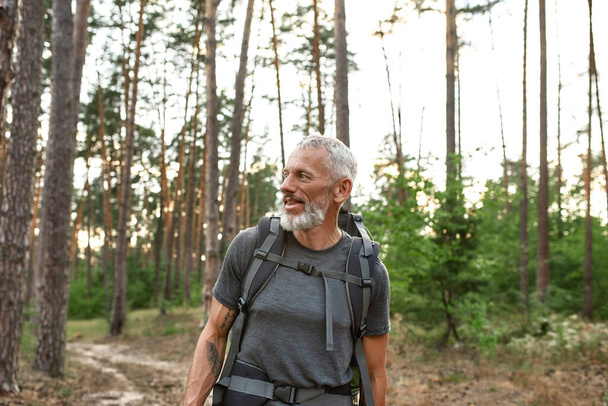 Smiling mature caucasian man walking alone in forest - Photo, Image