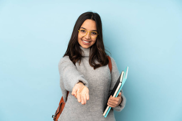 Young mixed race woman going to school isolated on blue background holding copyspace imaginary on the palm to insert an ad - Photo, Image