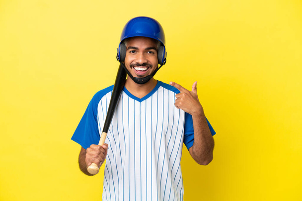 Jonge Colombiaanse latino man spelen honkbal geïsoleerd op gele achtergrond geven een duim omhoog gebaar - Foto, afbeelding