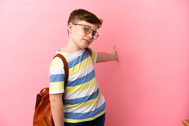 Little redhead caucasian boy isolated on pink background extending hands to the side for inviting to come - Φωτογραφία, εικόνα