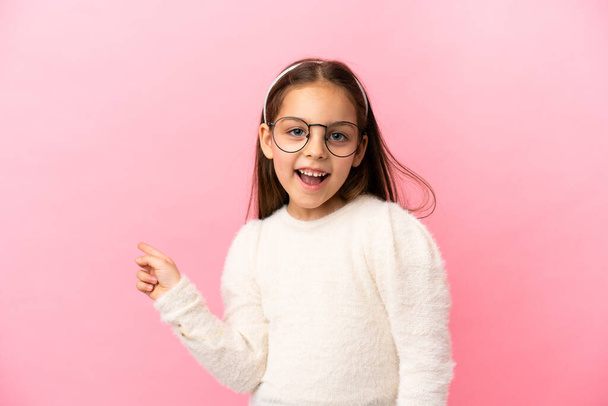 Little caucasian girl isolated on pink background surprised and pointing finger to the side - Foto, imagen