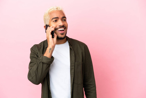 Young Colombian handsome man isolated on pink background keeping a conversation with the mobile phone - 写真・画像