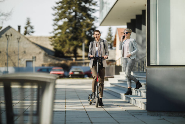 A young businesswoman riding an electric scooter on her way to work. - Foto, Bild