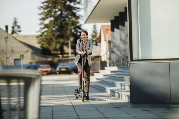 A young businesswoman going to work with an electric push scooter. - Foto, Bild
