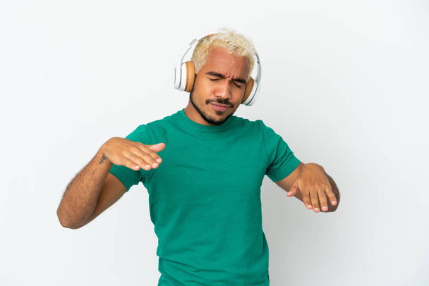 Joven colombiano guapo aislado sobre fondo blanco escuchando música y bailando - Foto, Imagen