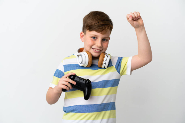 Ένα μικρό κοκκινομάλλικο αγόρι που κρατάει ένα παιχνίδι απομονωμένο σε λευκό φόντο γιορτάζοντας μια νίκη - Φωτογραφία, εικόνα