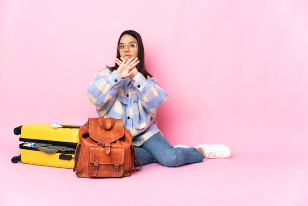 Podróżniczka z walizką, siedząca na podłodze i wykonująca gest zatrzymania się, by powstrzymać akcję. - Zdjęcie, obraz