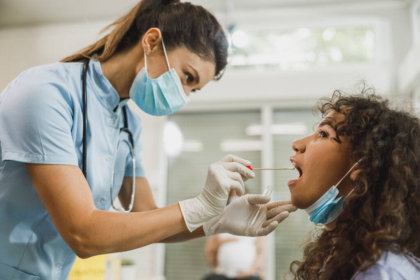 An African American teenager girl having swab medical test from throat during coronavirus pandemic. - Fotografie, Obrázek